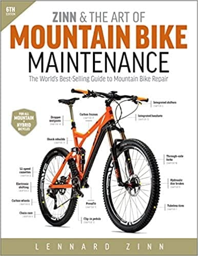 A person working on a mountain bike using the "Zinn & the Art of Mountain Bike Maintenance" guidebook as a reference.