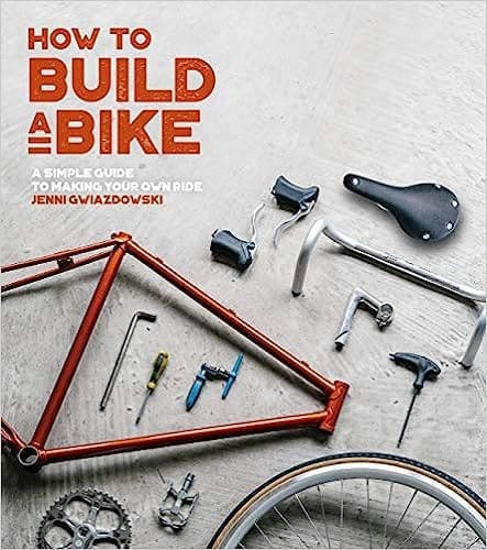 Cover image of the book 'How to Build a Bike: A Simple Guide to Making Your Own Ride', featuring a bicycle frame and parts blueprint design.