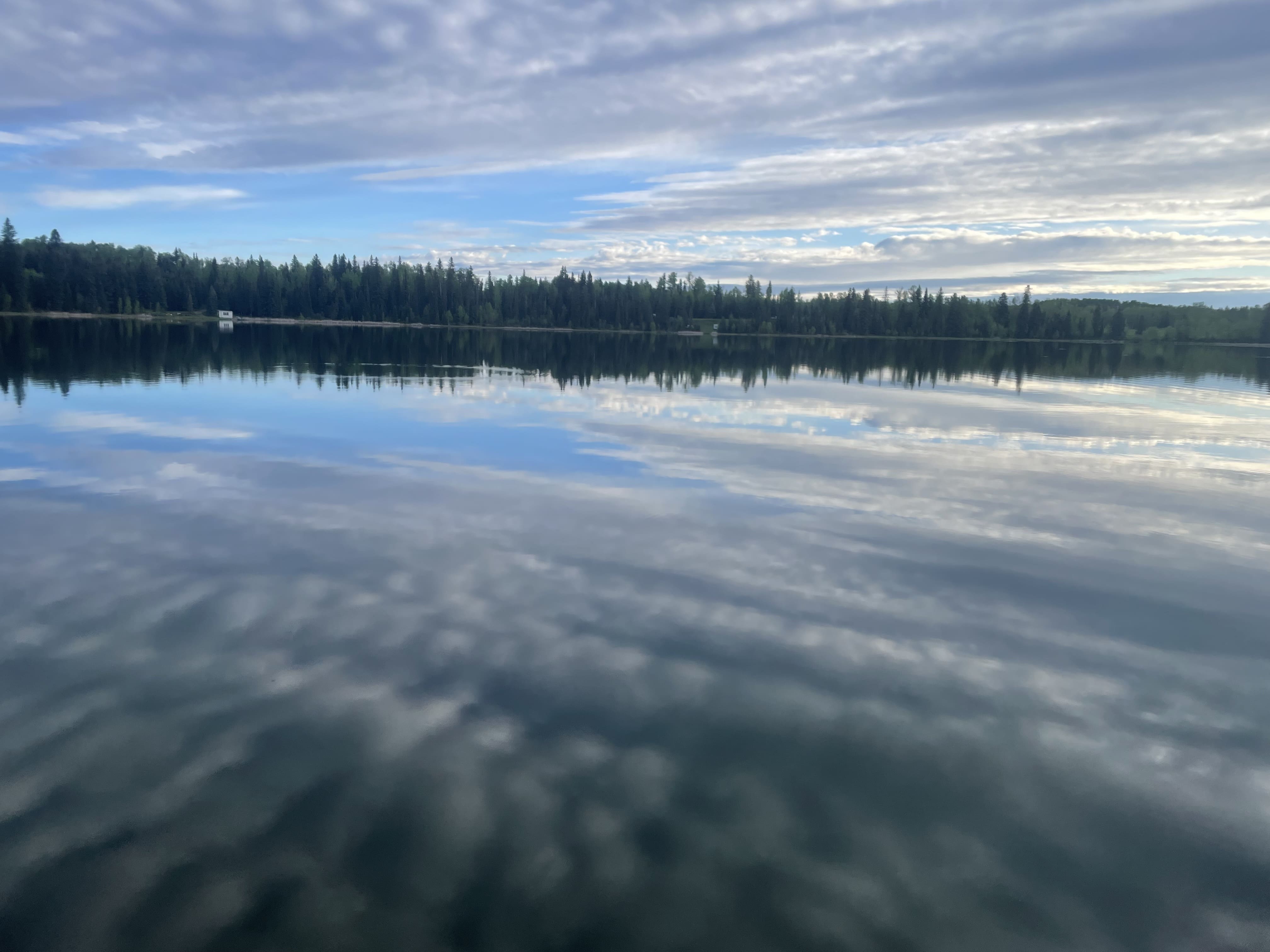 Reflection of clouds and shoreline trees in the calm waters of Strubel Lake.